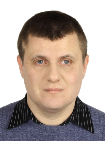 Чоловік з коротким темним волоссям і світлою шкірою, одягнений у синій светр поверх сорочки з чорним коміром у світлу смужку